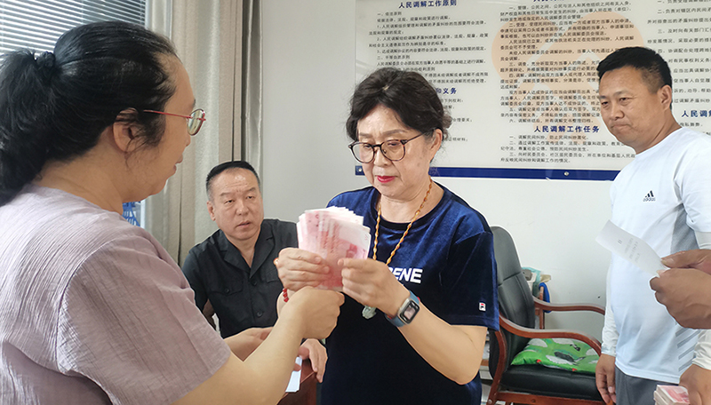 頭題片，5月30日,，某藥業(yè)公司按協(xié)議約定完成第一期履行義務(wù),，將十萬現(xiàn)金交到法院，調(diào)解員付菊（左一）清點(diǎn)無誤之后交到農(nóng)民工委托代理人徐某手中